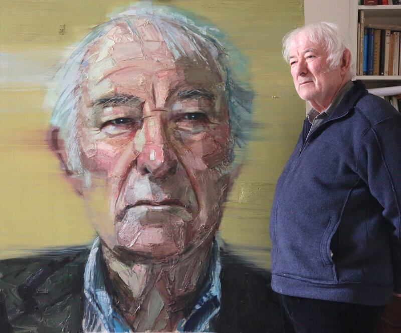The late Seamus Heaney poses alongside Colin Davidson's portrait of him