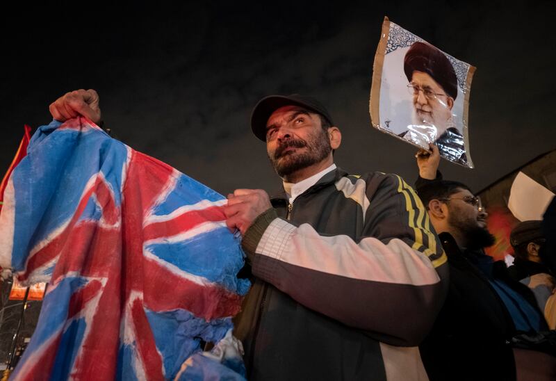 An Iranian protester holds a torn British flag while standing under a portrait of Iran's Supreme Leader, Ayatollah Ali Khamenei, during an anti-US and anti-British protest in front of the British embassy in Tehran, Iran, on January 12th, 2024. Photograph: Morteza Nikoubazl/NurPhoto via Getty Images