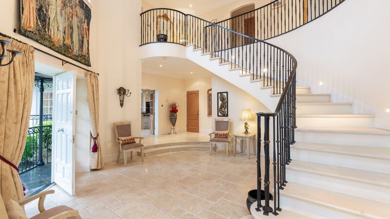 The double-height entrance hall gets its drama from its curved staircase with black wrought iron rails and the tall windows throwing light into the hall and landing