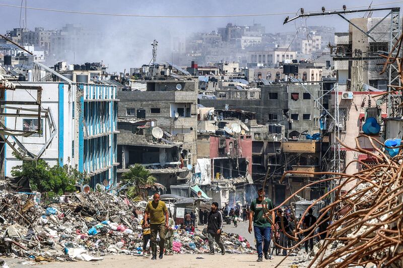 People walk past a mound of trash and destroyed buildings as smoke rises during Israeli bombardment in Jabalia on May 14th. Photograph: AFP via Getty