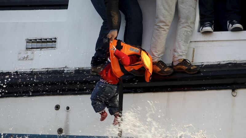 A refugee prepares to hand over a toddler to a volunteer lifeguard off Lesbos. Photograph: Giorgos Moutafis/Reuters