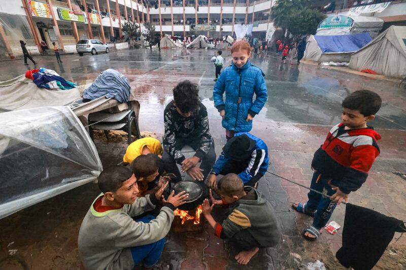 Palestinian children warm themselves around a fire at their makeshift  camp in a schoolyard in Rafah, southern Gaza Strip, on December 13th, 2023, as battles continue between Israel and Palestinian militant group Hamas. Photograph: Mohammed Abed/AFP/Getty 
