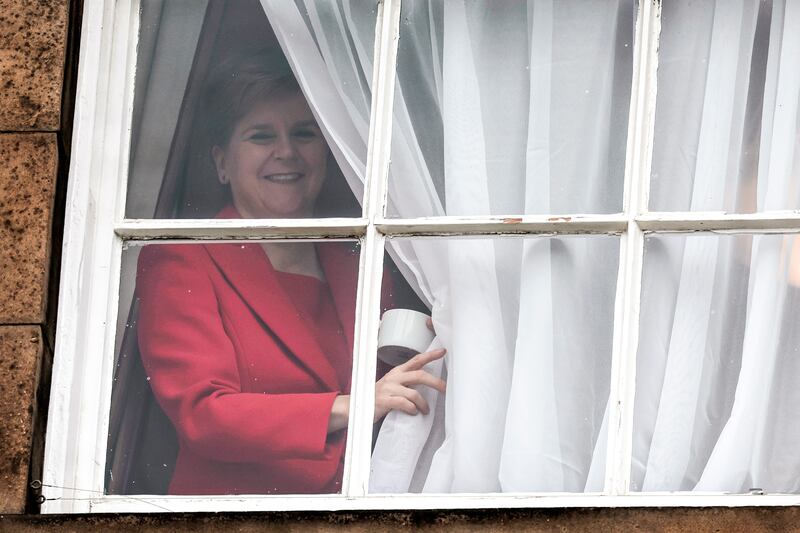 Nicola Sturgeon waves from a window, after holding a press conference to announce her resignation, as people gather outside of Bute House in Edinburgh, UK. Photograph: Jeff J Mitchell/Getty Images