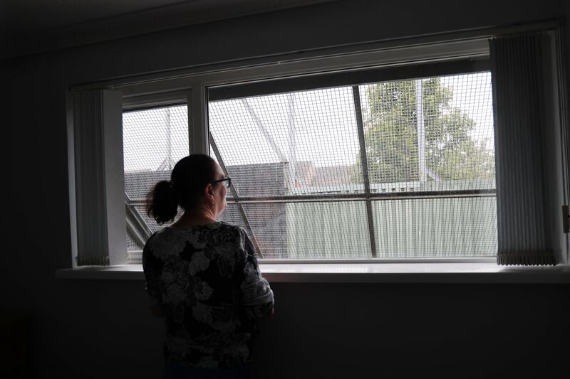 Jean Canavan looks out of a bedroom window towards the ‘cage’ and peace wall behind her home in Bombay Street in the Falls Road area of west Belfast. Photograph: Bryan O’Brien