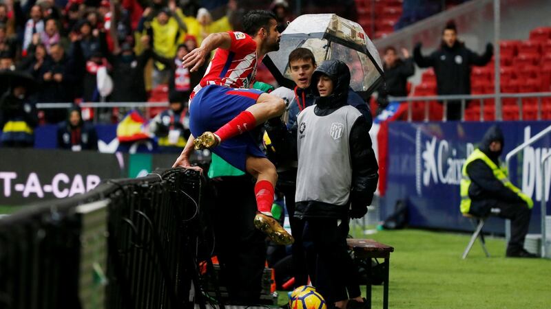 Costa hurdles the advertising hoarding to celebrate with fans. Photo: Javier Barbancho/Reuters