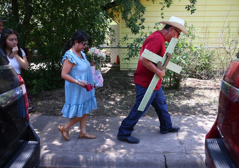 A man carries a cross he made as his wife carries flowers to pay their respects to the 21 victims of the Robb Elementary School shooting in Uvalde, Texas (Kin Man Hui/The San Antonio Express-News via AP)