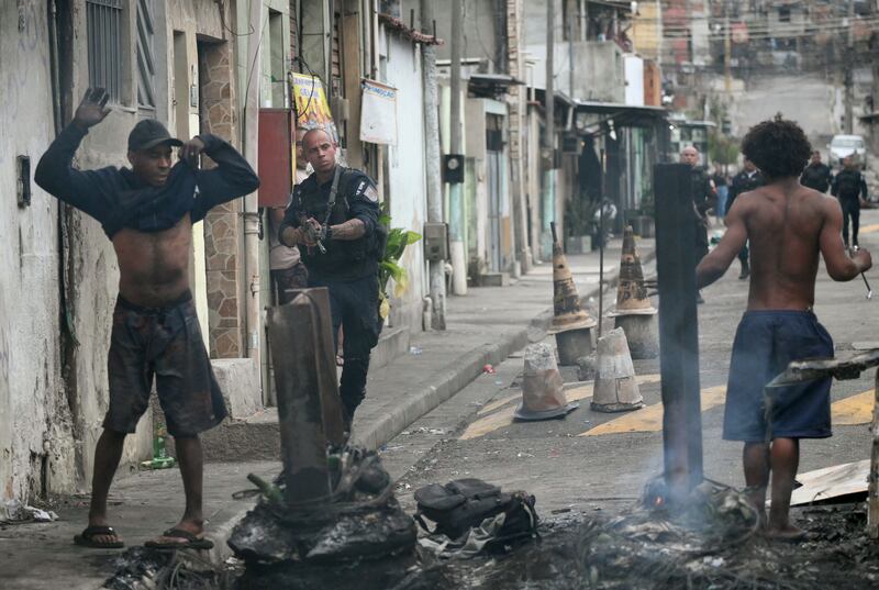 A police officer holds his gun up next to residents on a barricade during the Operacao Contencao (Operation Containment) at the Vila Cruzeiro favela, in the Penha complex, in Rio de Janeiro, Brazil, on October 28, 2025. Photograph: Mauro Pimentel/Getty Images     