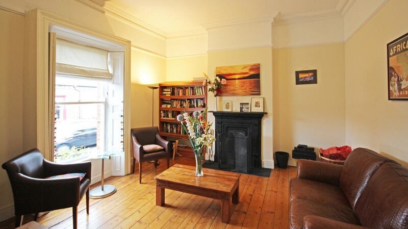 The livingroom at 28 Curzon Street, Dublin 8 has a cast-iron fireplace, centre rose, polished wooden floor and shutters on the sash window