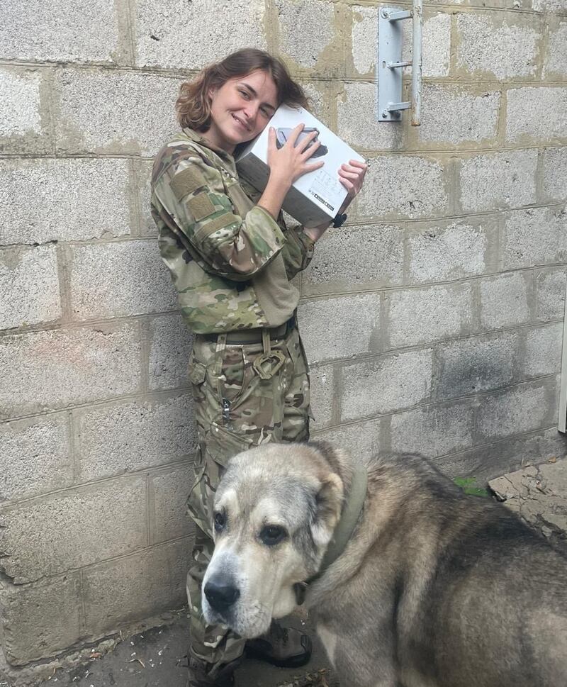 Lt Yulia Mykytenko hugs a newly received drone, with an army dog at her feet. She commands a drone unit with the 54th mechanised brigade.