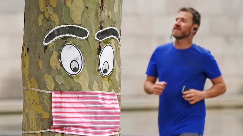 A man runs past a tree with a face mask and eyes stapled to it in Melbourne, Australia on Sunday.  Photograph: Scott Barbour/EPA