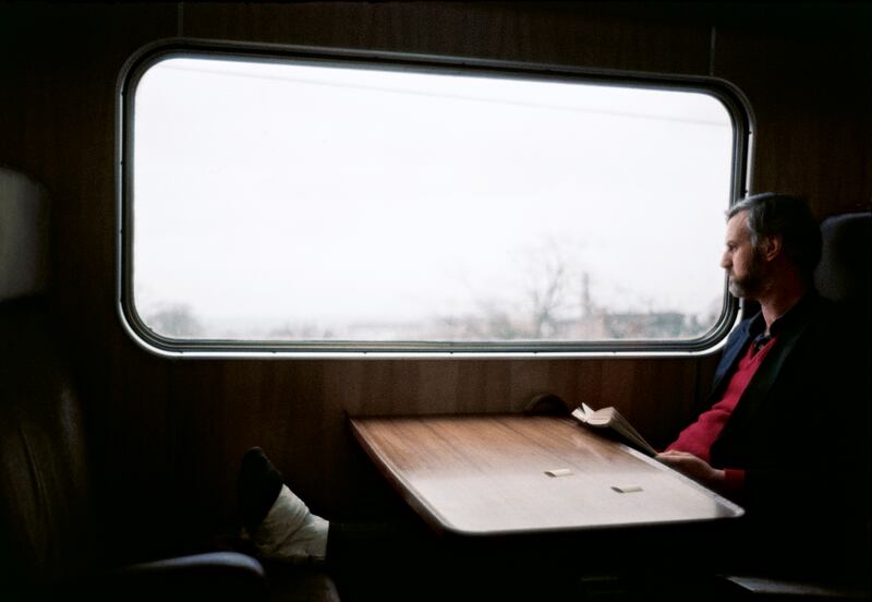 A man with an injured foot reads The Dogs of War by Frederick Forsythe on a train in Northern Ireland in 1976.