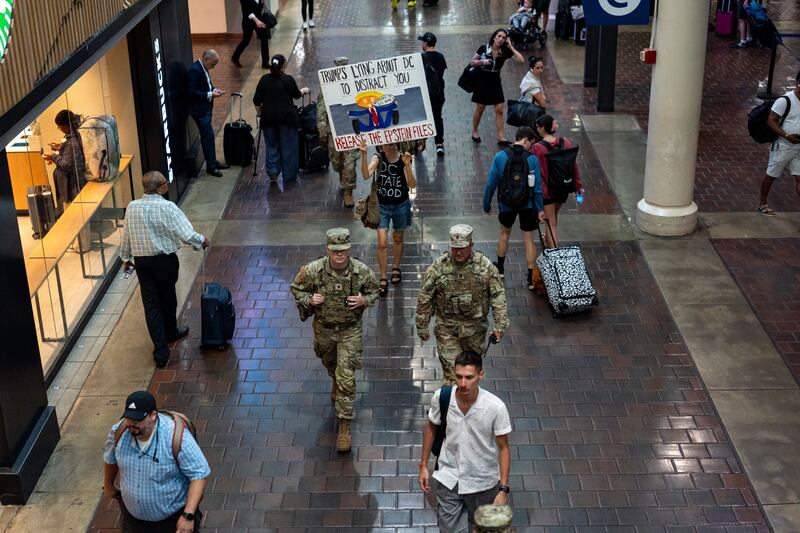 A protester holds a sign and follows members of the National Guard as they patrol Union Station in Washington DC. Photograph: Kent Nishimura/The New York Times
                      