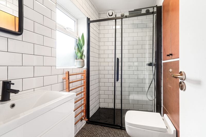 The sleek, contemporary shower room sits off the kitchen with white metro tiles and black and brass-coloured fittings.