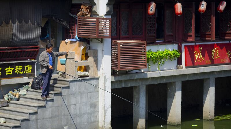 A man is standing on the stairs of a tea house and fishing out of the river. Photograph: iStock