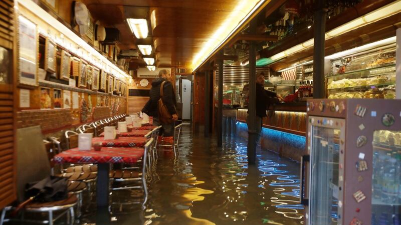 People stand inside a flooded cafe  in Venice  on Tuesday. The high tide reached a peak of 127cm (4.1ft) at 10:35am while an even higher level of 140cm(4.6ft) was predicted for later Tuesday evening.  Photograph: Luca Bruno/AP