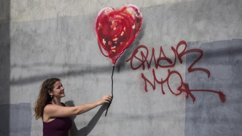 A woman poses with a piece of street art, which depicts a heart-shaped balloon covered in bandages and was allegedly done by the street artist Banksy in the Red Hook neighbourhood of the Brooklyn borough of New York City. The piece was defaced with red spray paint shortly after being completed. Photograph: Andrew Burton/Getty Images