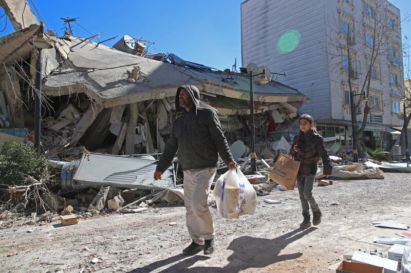 People carry aid materials next to a collapsed building in Adiyaman, Turkey, on Thursday, following last week's powerful earthquake. Photograph: Tolga Bozoglu/EPA-EFE