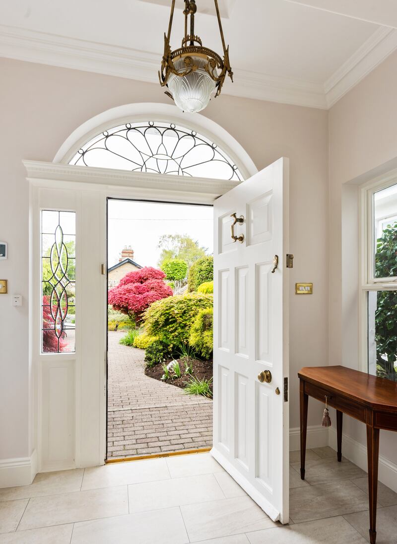 The front door is topped by a fanlight and opens into a tiled porch and entrance hall, where steps lead off to the wings.