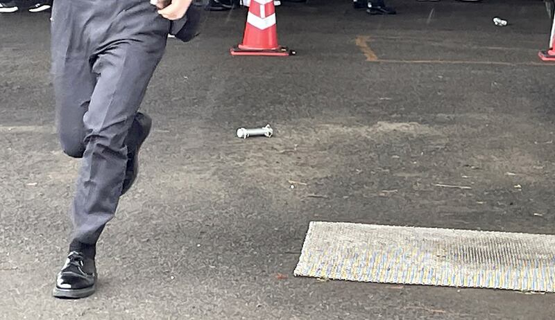 A cylinder-shaped object, believed to have been thrown during a campaign appearance by Japan's prime minister Fumio Kishida, lies on the ground as an official runs past in Wakayama earlier today. Photograph: JIJI Press/AFP/Getty 
