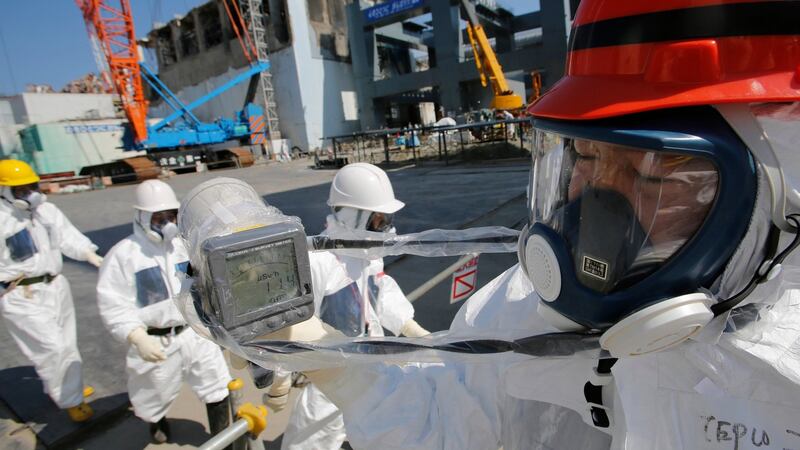A radiation monitor reads 1t the No. 4 reactor building, backgroun14.00 microsieverts per hour as members of the media and Tokyo Electric Power Co (Tepco) employees, wearing protective suits and masks, visid center, and the construction of a storage unit for melted fuel rods, background right, at the company's Fukushima Dai-Ichi nuclear power plant in Okuma, Fukushima Prefecture last Wedensday.  Photograph: Issei Kato/Pool via Bloomberg