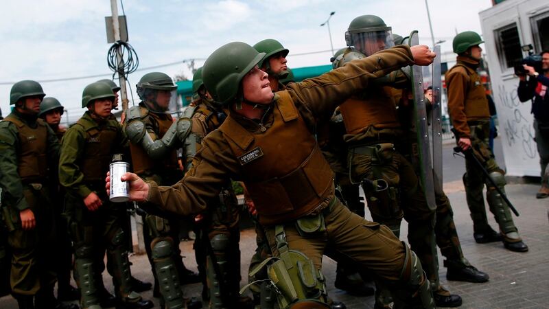 A police officer throws a tear gas cannister during clashes with protesters at Plaza de Maipu in Santiago. Photograph: Pablo Vrea/AFP via Getty