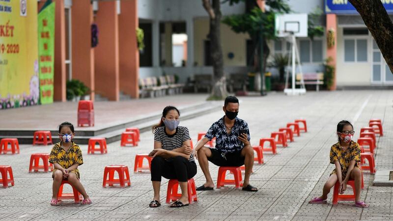 A family sit on plastic stools as they wait to be tested in Hanoi. Photograph:  Manan Vatsyayana/AFP via Getty Images